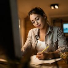 Hispanic young lady sitting at table studying notes